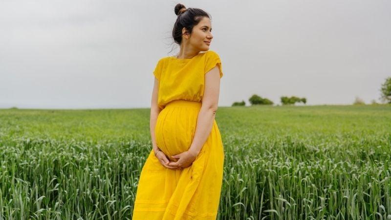 A woman pregnant from egg donation standing in a field
