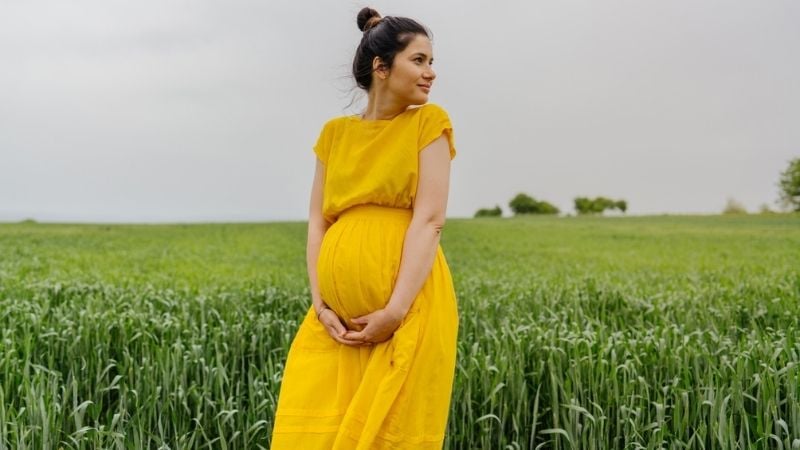 A woman pregnant from egg donation standing in a field
