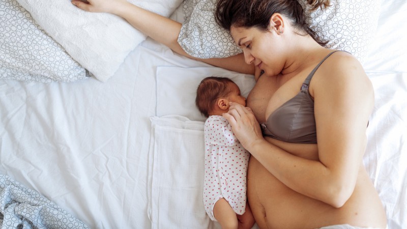 En mor, som ligger i sengen og ammer sit barn