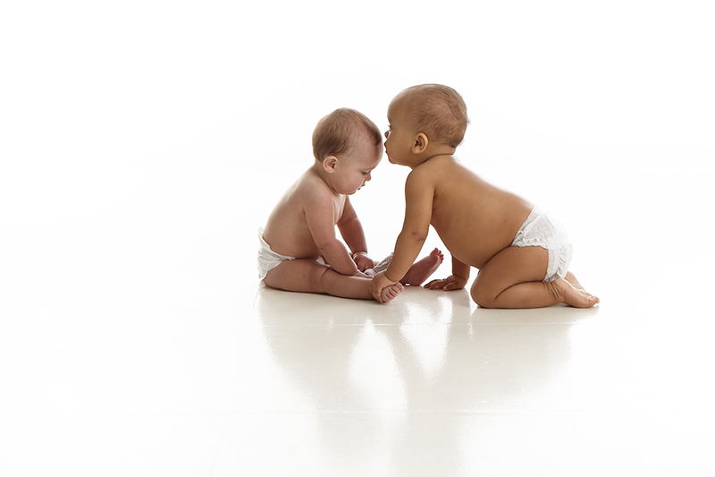 Twee baby's zitten tegen over elkaar tegen een witte achtergrond – Foto uit de Cryos-persmap. 